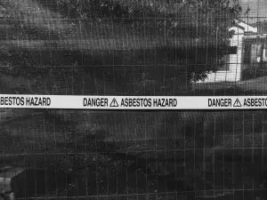 Asbestos hazard warning tape on construction site fence in black and white